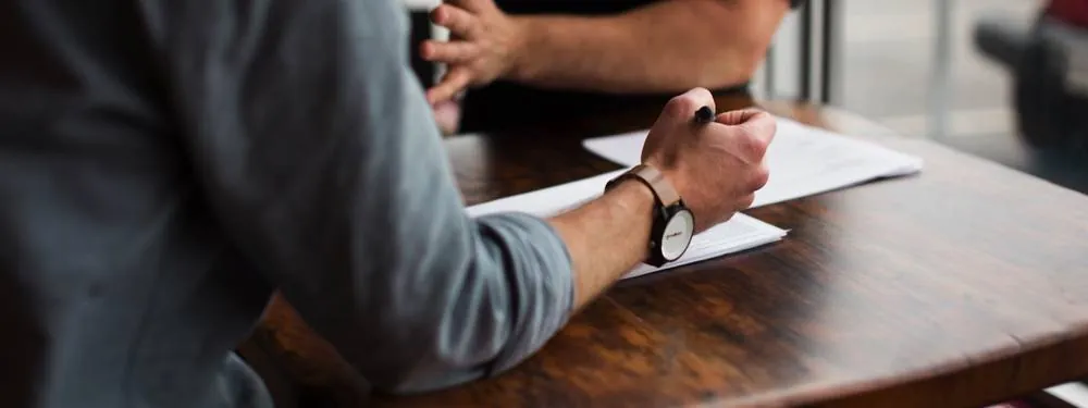 Two people talking across a table with paperwork between them.